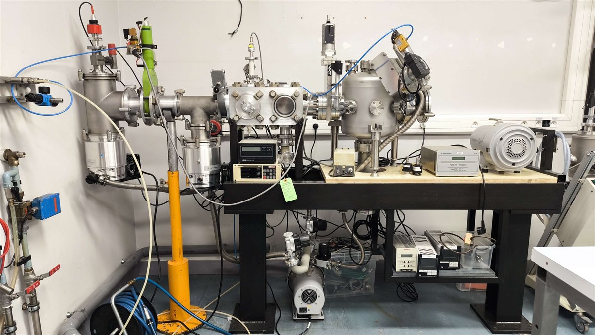 Enceinte sous vide sur bâti : croix de pompage, vannes, jauges et pompes turbomoléculaires raccordées à une ligne.