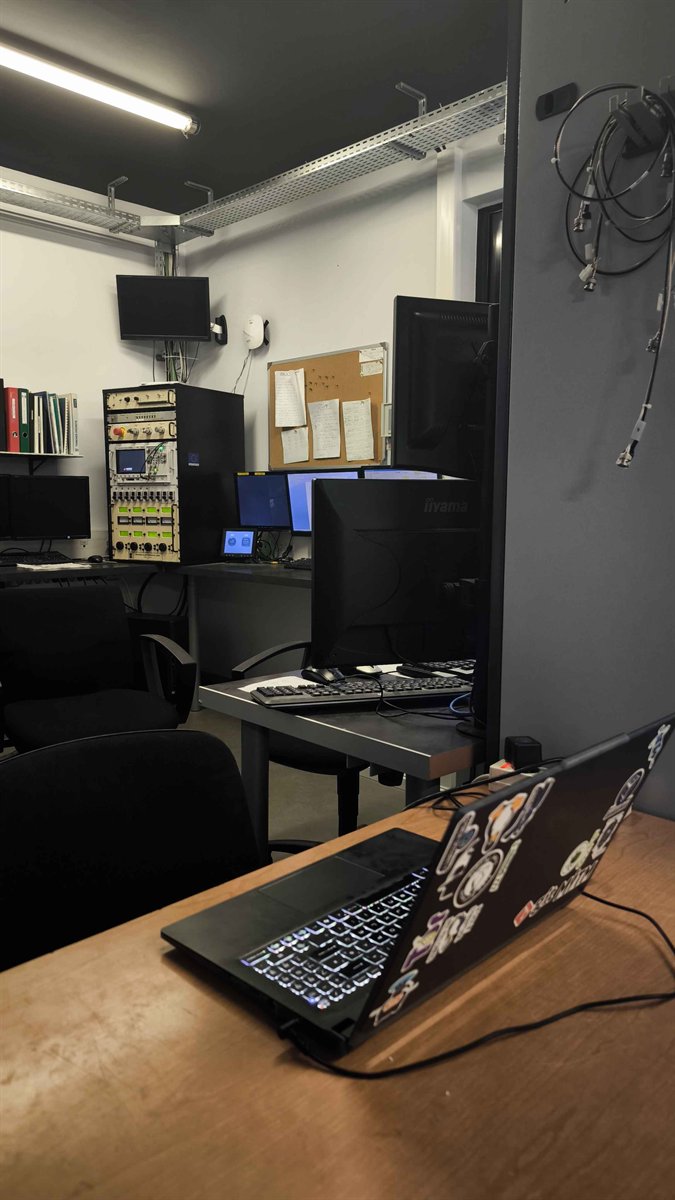Salle de conduite : baie de commande et écrans au fond, postes de travail et ordinateur portable au premier plan.